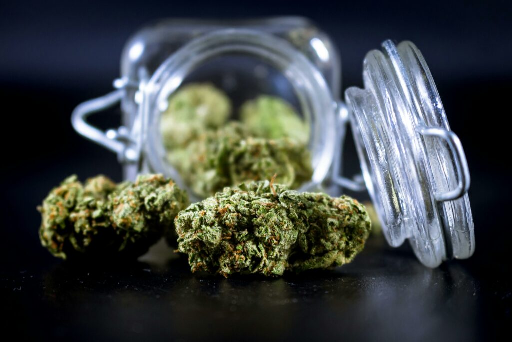 High-quality image of cannabis buds partially spilling from an open glass jar.
